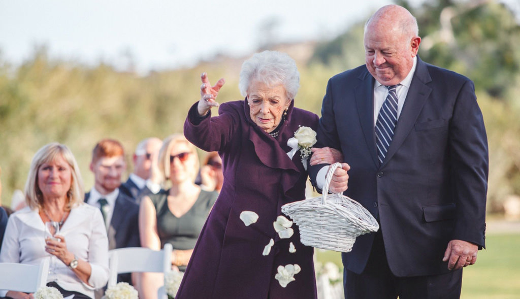 A grandmother flower girl walking down the aisle tossing flower petals.