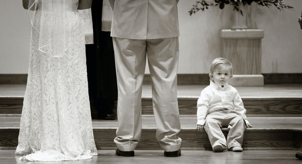 A ring bearer sitting down during a long catholic wedding ceremony.