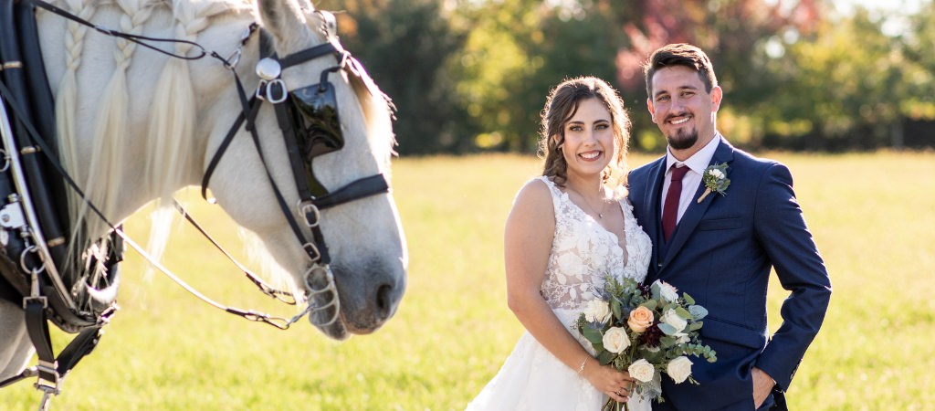 A bride and groom posing with a horse on their wedding day